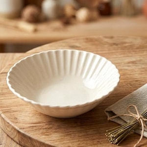 May include: A white, fluted ceramic bowl sits on a wooden surface, next to a bundle of lavender tied with twine and a linen napkin. The bowl has a scalloped rim and a smooth interior. The scene evokes a rustic, farmhouse aesthetic.