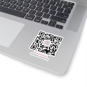 May include: A black and white QR code sticker with the text "WARNING contains creativity" on a silver laptop.
