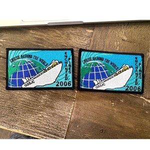 May include: Two rectangular embroidered patches featuring a white cruise ship, a blue and green globe, and the text "CRUISE AROUND THE WORLD", "ENCHANTED PINES", and "2006". Each patch has a black border and "GSSJC" printed on the ship hull.