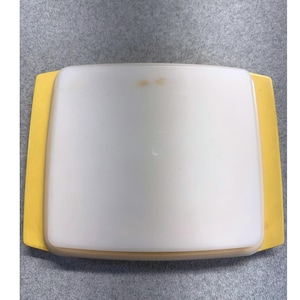 May include: A rectangular storage container with a translucent white lid and a solid yellow base featuring integrated side handles. The lid has a smooth, matte surface with two small, faint brownish spots visible near the top center edge.