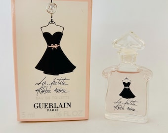 May include: A miniature perfume bottle and box set. The box is light pink with a black dress illustration and the text "La petite Robe noire". The bottle is clear with a pink liquid and a dress illustration.