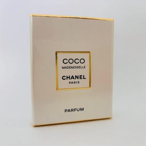 Op de afbeelding: Een rechthoekige parfumdoos in gebroken wit met een gouden rand. De voorkant toont de tekst "COCO MADEMOISELLE CHANEL PARIS PARFUM" in een goudomrand rechthoek.
