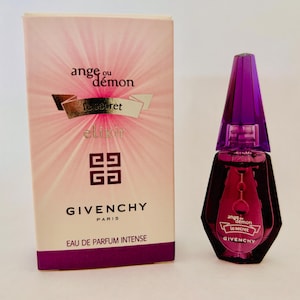 Könnte beinhalten: Ein Parfümflaschen- und Box-Set. Die Flasche hat eine dunkelrote, geometrische Form mit einem lila Verschluss. Die Box ist rosa mit den Worten "ange ou démon le secret elixir" und dem Givenchy-Logo. Die Worte "EAU DE PARFUM INTENSE" sind ebenfalls sichtbar.