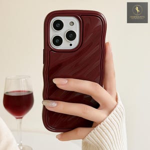 May include: A burgundy phone case with a textured, wavy design. The case has a glossy finish and a camera cutout. The phone case is held in a hand, with a glass of red wine in the background.