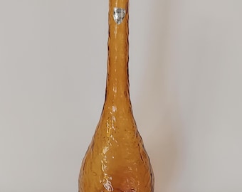 May include: Amber-colored glass vase with a textured surface. The vase has a long, slender neck and a bulbous base. A small, silver label is affixed near the top. The vase is likely vintage and suitable for displaying flowers or as a decorative piece.