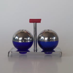 May include: A retro salt and pepper set. The shakers have a silver top and a blue base, and are held in a silver metal tray with a red handle. A classic kitchen accessory, the shakers are spherical.