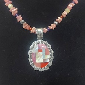 May include: A silver pendant necklace with a mosaic design. The pendant features a geometric pattern of pink, red, and white mother-of-pearl pieces. The necklace has a beaded strand of pink, purple, and orange stones.