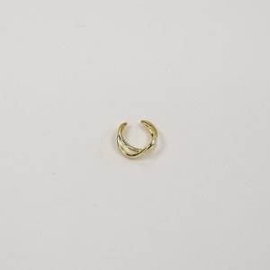 Könnte beinhalten: Ein goldfarbener Ohrklemme mit einem Kreuzdesign. Das Schmuckstück ist ein schlichtes, elegantes Accessoire. Der Ohrklemme ist so konzipiert, dass er ohne Piercing am äußeren Ohr getragen werden kann. Das Metall hat ein glänzendes Finish.