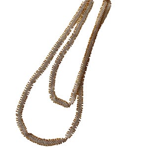 May include: A gold-toned necklace with a zig-zag design. The necklace is made of small, closely-set, sparkling elements, creating a textured appearance. The chain is draped against a white background.