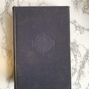 May include: A dark blue hardcover book with the name "O. Henry" embossed on the cover within a decorative emblem. The book's cover is a solid, muted blue, and the edges are slightly worn.