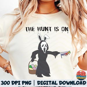Puede incluir: Camiseta color crema con el texto "THE HUNT IS ON" sobre un gráfico de una figura con túnica negra y orejas de conejo, sosteniendo un cuchillo con una hoja arcoíris y una cesta de huevos de Pascua. Descarga digital.