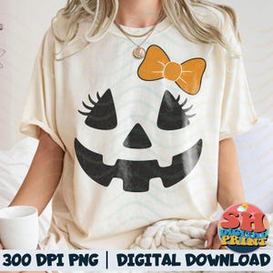 May include: Cream-colored t-shirt featuring a Halloween-themed jack-o'-lantern face design. The design includes black eyes with eyelashes, a triangular nose, and a smiling mouth. An orange bow is above the eyes. The text "300 DPI PNG | DIGITAL DOWNLOAD" is at the bottom.
