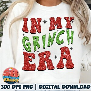 May include: White sweatshirt featuring the phrase "IN MY GRINCH ERA" in red and green glitter lettering. The design includes small black star accents. The bottom of the image includes the text "300 DPI PNG | DIGITAL DOWNLOAD".