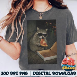 Puede incluir: Camiseta gris oscuro con un gráfico de un mapache con gafas de sol comiendo pizza. El mapache está sentado junto a una caja de pizza abierta. El texto "300 DPI PNG | DIGITAL DOWNLOAD" está en la parte inferior.