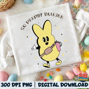 Puede incluir: Sudadera blanca con un diseño de conejo de dibujos animados amarillo y el texto "So Peepin' Boujee". El conejo lleva un bolso cruzado y un vaso rosa. El diseño incluye pequeños acentos de estrellas amarillas.