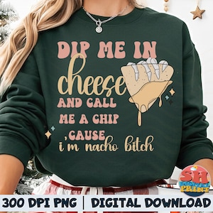 May include: Dark green sweatshirt with the text "Dip me in cheese and call me a chip, cause I'm nacho bitch" in pink and tan lettering. A graphic of a tortilla chip with melted cheese is also featured.