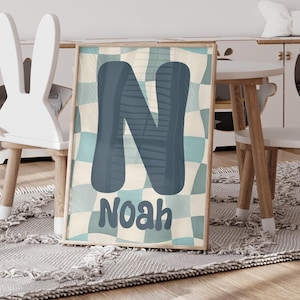 Könnte beinhalten: Gerahmter Druck mit einem großen blauen Buchstaben "N" vor einem karierten Hintergrund aus hellblauen und beigen Quadraten. Der Name "Noah" ist darunter in passender blauer Schrift gedruckt. Der Druck wird in einem Kinderzimmer ausgestellt.
