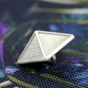May include: A white pyramid-shaped button with a textured surface. The button is made of plastic and has a flat back.