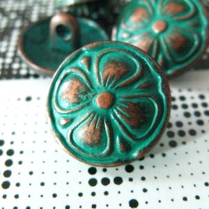 Op de afbeelding: Een turquoise knoop met een koperen bloemdessin. De knoop heeft een reliëf, gegraveerde bloem met vijf bloemblaadjes en een koperen centrum. De knoop heeft een gat in het midden om te naaien.