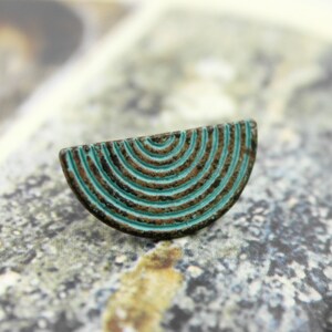 May include: A half-circle shaped metal charm with a turquoise blue and brown concentric circle design.
