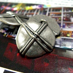 May include: Two silver metal cufflinks with a criss-cross design. The cufflinks are on a dark background.