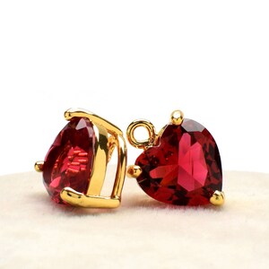 Puede incluir: Dos abalorios dorados en forma de corazón con detalles de cristal rojo. Los abalorios tienen un bucle en la parte superior para sujetarlos a joyas.