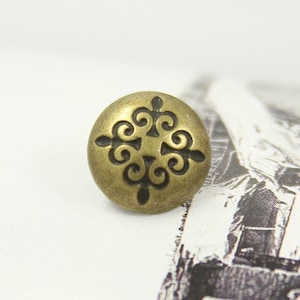 May include: A gold-toned metal button with a decorative black design. The button has a round shape and a raised design.