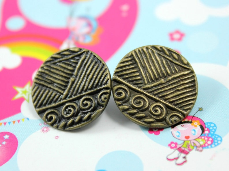 Puede incluir: Un par de pendientes redondos de color bronce con un dise&ntilde;o texturizado. Los pendientes presentan un patr&oacute;n de espiral y un dise&ntilde;o geom&eacute;trico.