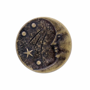 May include: A gold-toned metal button featuring a crescent moon design with a star. The moon has a face and the background is dark brown.