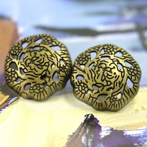 May include: Two gold-toned metal buttons with a floral design. The buttons have a circular shape with a raised, intricate pattern of flowers and leaves.