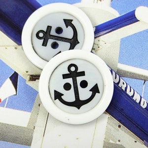 May include: Two white buttons with black anchor designs. The anchors have a simple, classic design with a crossbar and a ring at the top.