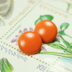 May include: Two bright orange round buttons on a white background with a floral design. The buttons are smooth and glossy.