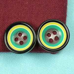 Puede incluir: Dos botones rayados en negro y verde con cuatro agujeros cada uno. Los botones tienen una raya amarilla y una raya blanca.