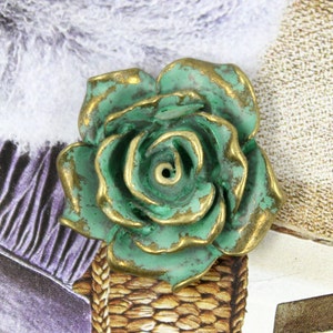 May include: A green and gold metal rose with a detailed, textured surface. The rose has a hole in the center, suggesting it may be used as an incense burner.