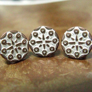 May include: Three round, silver-colored buttons with a brown border. Each button has a raised, white, starburst design with a circle in each point.