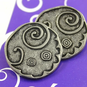 May include: Two silver-toned metal buttons with a swirl design. The buttons have a textured surface and a raised edge.