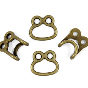 May include: Four antique gold-toned metal clasps with two holes each. The clasps are designed to be used for attaching straps or belts.