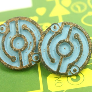 May include: Two round, blue and brown earrings with a circular pattern. The earrings have a distressed, aged look.