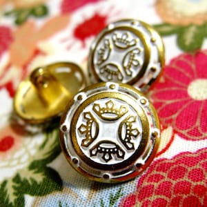 May include: Two gold-colored buttons with white centers. The buttons have a decorative design of four crowns.