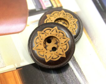 May include: Two brown wooden buttons with a decorative floral design in a light brown color. The buttons have two holes.