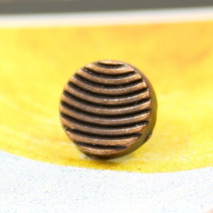 May include: A round, copper-colored button with a textured, ribbed design.