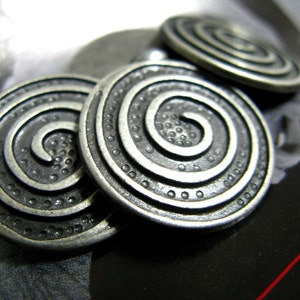 Op de afbeelding: Drie zilverkleurige metalen knopen met een spiraalvormig ontwerp. Elke knop heeft een reliëf, getextureerd spiraalpatroon.