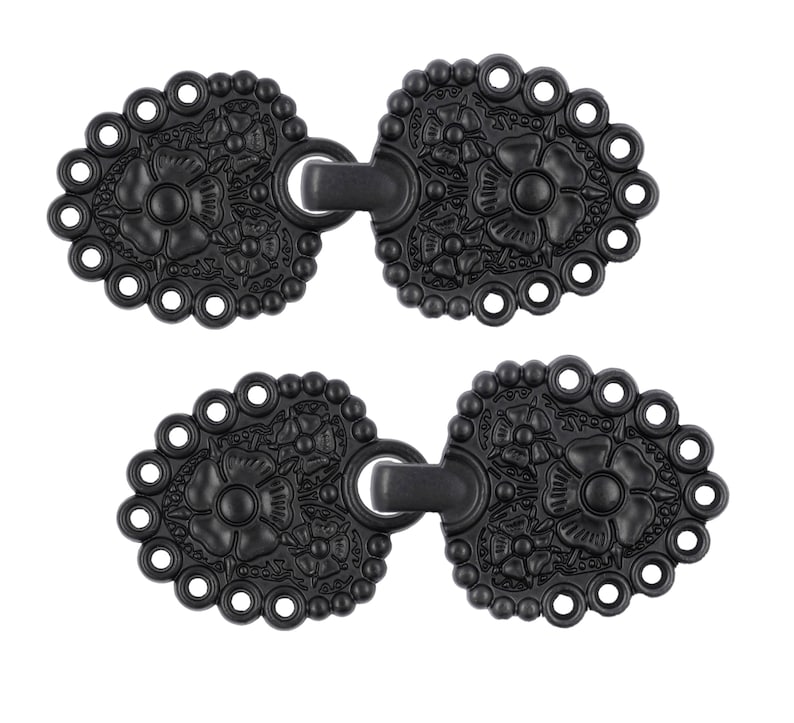 May include: Two black metal decorative clasps with a floral design. Each clasp has a loop on the side and a hook on the other side.