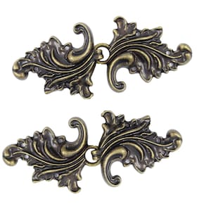 May include: Two ornate metal clasps with a floral design. The clasps are a dark bronze color and have a decorative loop on each side.