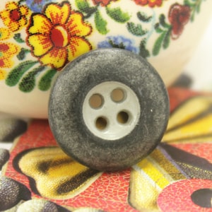 May include: A large, grey, four-hole button with a white centre.