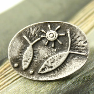 May include: Silver oval pendant with two stylized fish and a sun design.