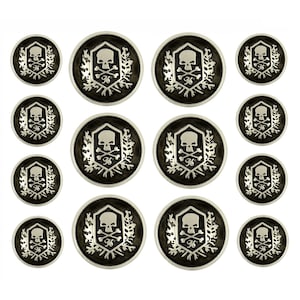 Może przedstawiać: Zestaw 12 srebrnych guzików z motywem czaszki i skrzyżowanych kości. Guziki są czarne z motywem czaszki i skrzyżowanych kości w kolorze srebrnym. Guziki są w różnych rozmiarach.