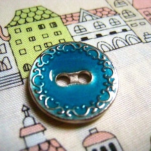 Peut inclure: Un bouton argenté avec un centre en émail bleu et une bordure argentée décorative. Le bouton a un design à deux trous.