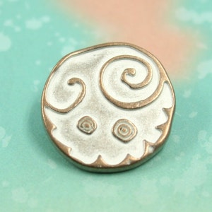 May include: White metal button with a raised design of two spirals and two smaller circles. The button has a bronze-coloured edge.