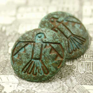May include: Two turquoise blue metal buttons with a stylized bird design. The buttons have a distressed, aged look.